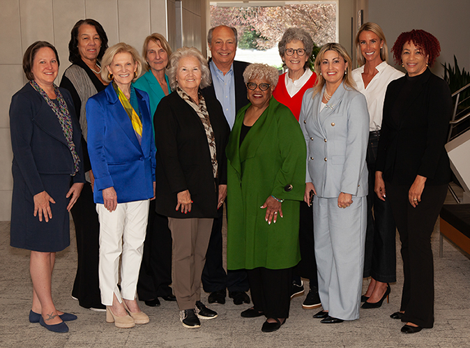 A group of women standing together in a well-lit room, engaged in conversation and smiling at each other.